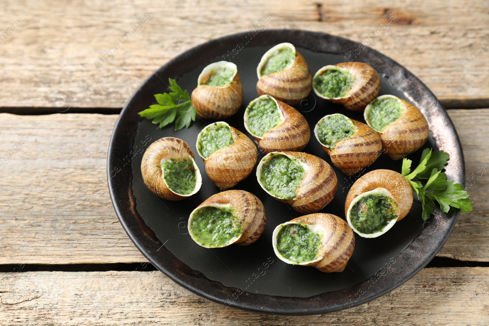 Photo of Delicious cooked snails with parsley on wooden table