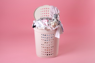 Photo of Laundry basket with baby clothes and soft toy on light pink background