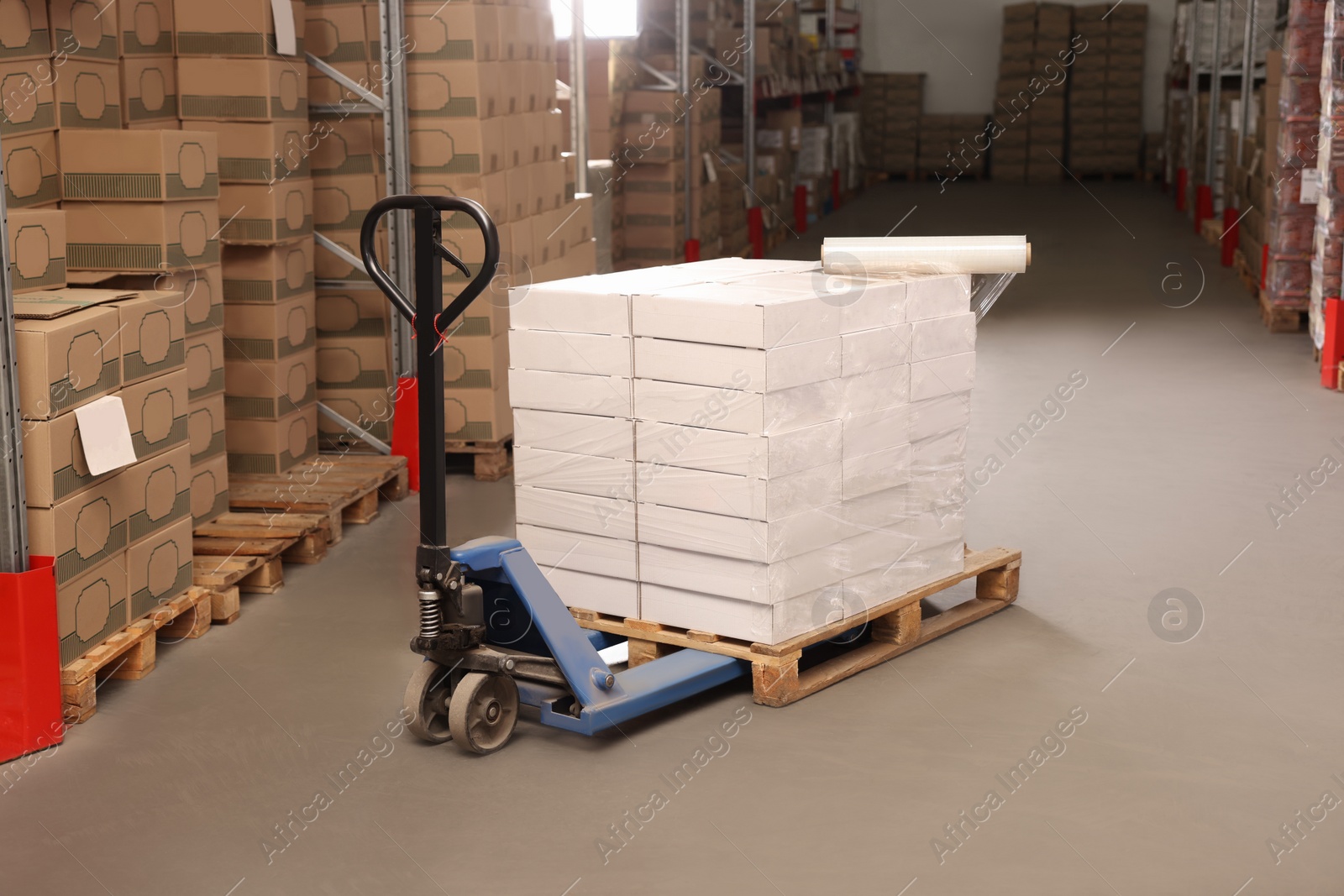 Photo of Manual pallet truck with stacked boxes and roll of stretch wrap in warehouse