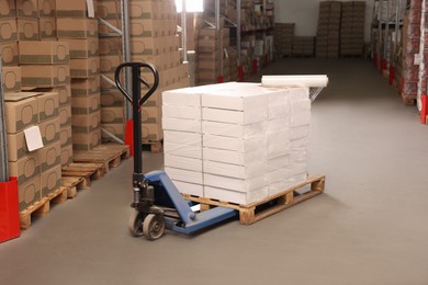 Photo of Manual pallet truck with stacked boxes and roll of stretch wrap in warehouse