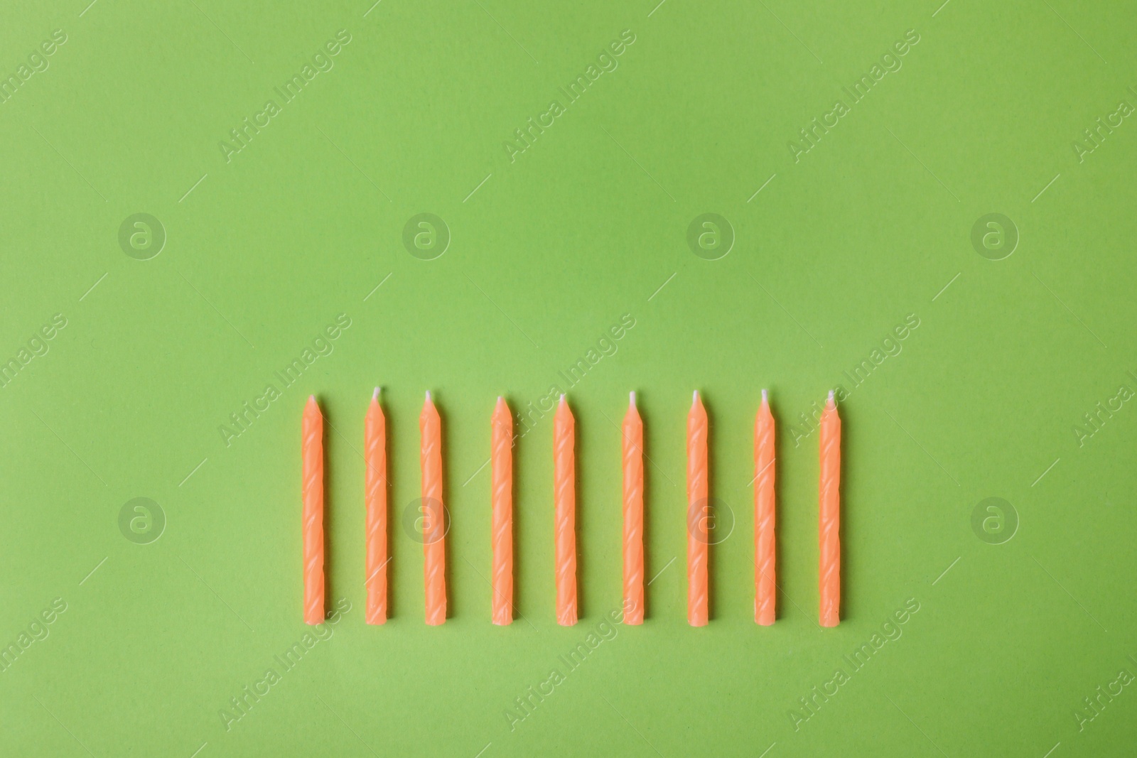 Photo of Orange birthday candles on green background, top view with space for text