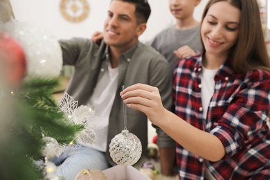 Happy family with cute child decorating Christmas tree together at home, focus on hand