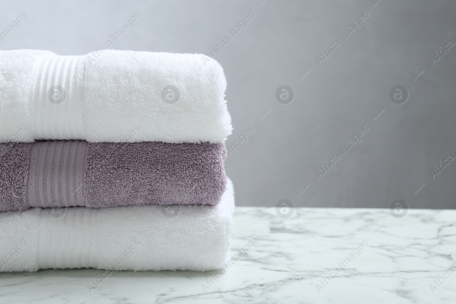 Photo of Stack of folded terry towels on white marble table, closeup. Space for text
