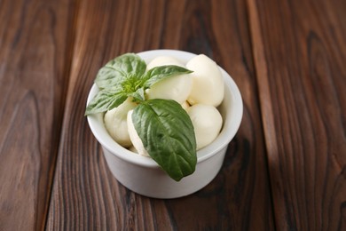 Tasty mozarella balls and basil leaves in bowl on wooden table, closeup