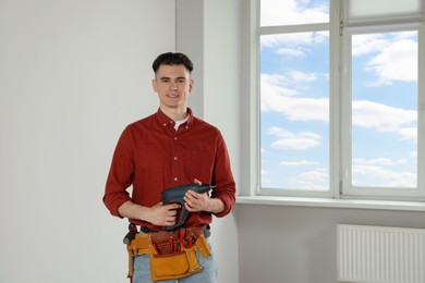Photo of Handyman with electric screwdriver and tool belt in empty room