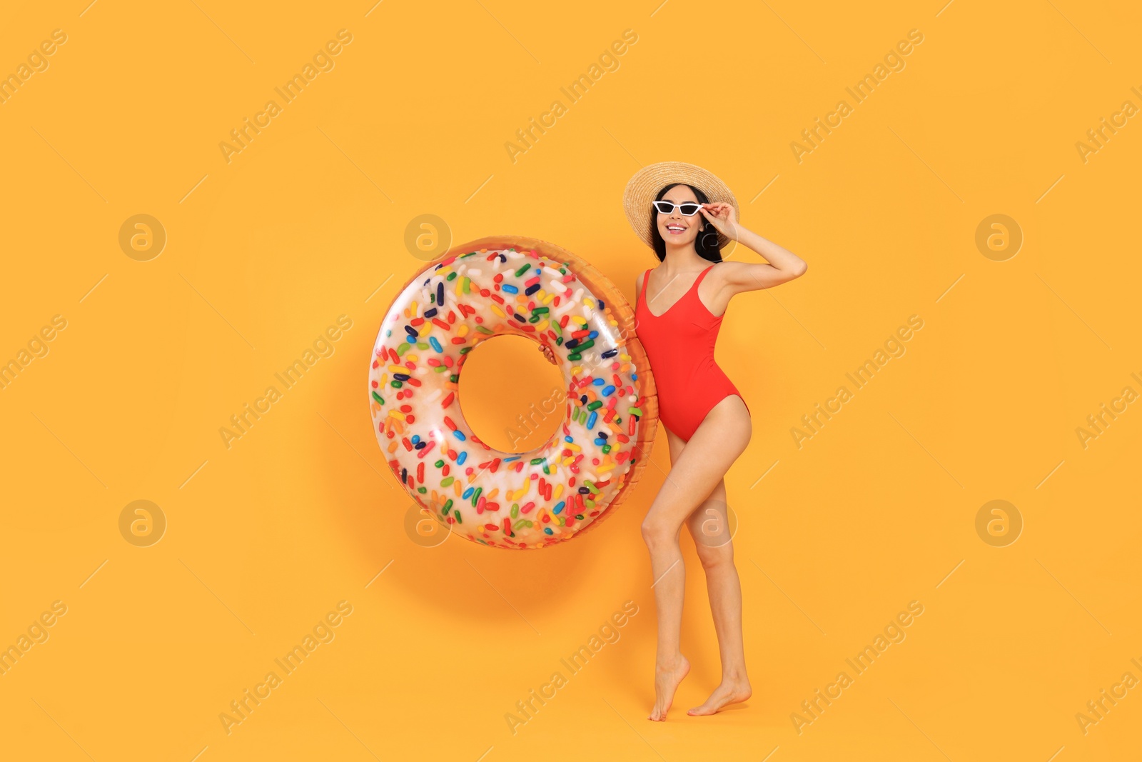 Photo of Happy young woman with beautiful suntan, hat and sunglasses holding inflatable ring against orange background