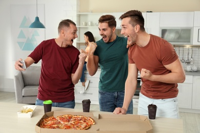 Group of friends with tasty food laughing together in kitchen