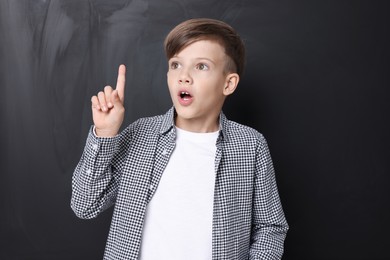 Photo of Back to school. Surprised boy pointing upwards near chalkboard