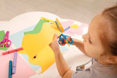 Little girl cutting color paper with scissors at table, above view