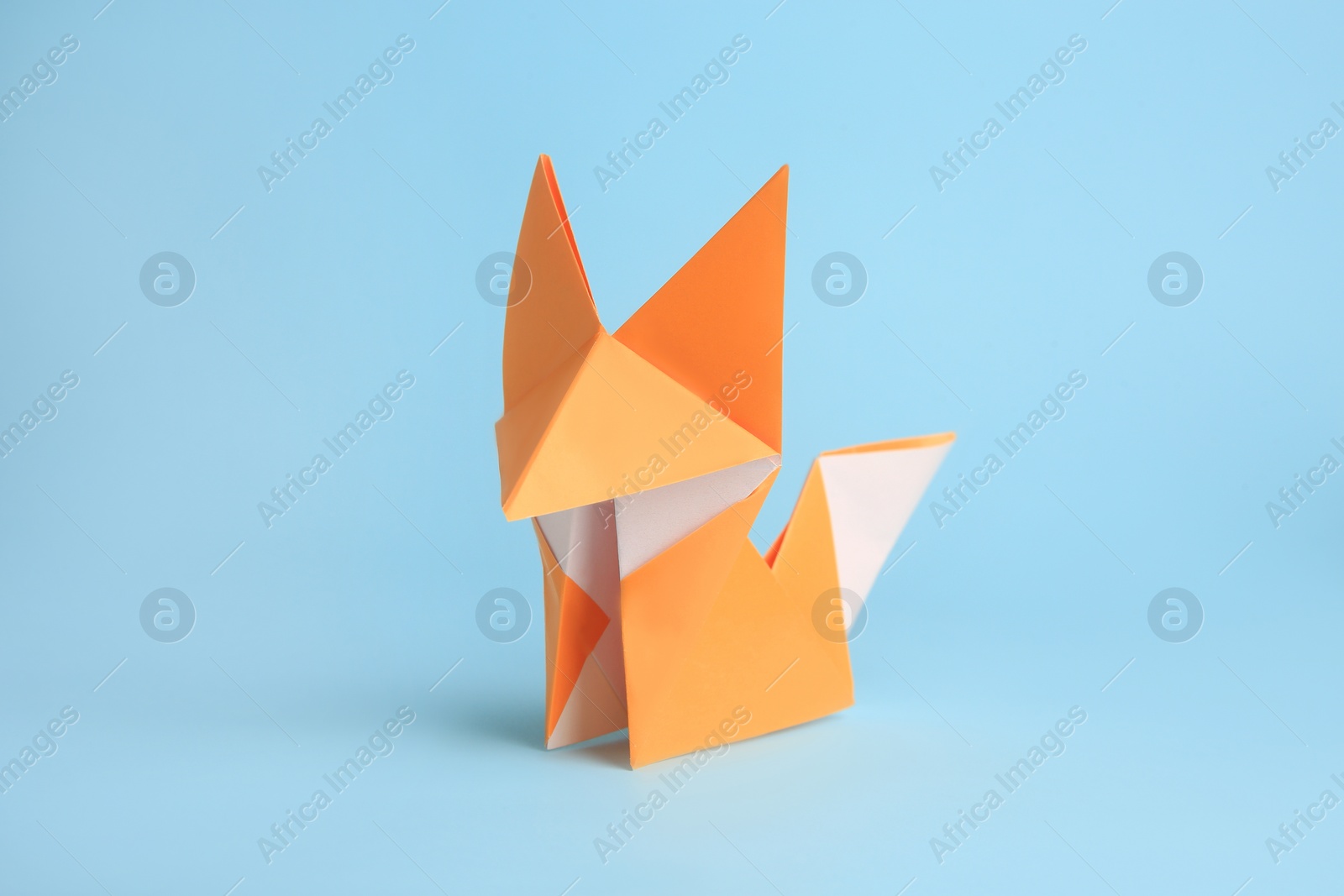 Photo of Origami art. Handmade orange paper fox on light blue background