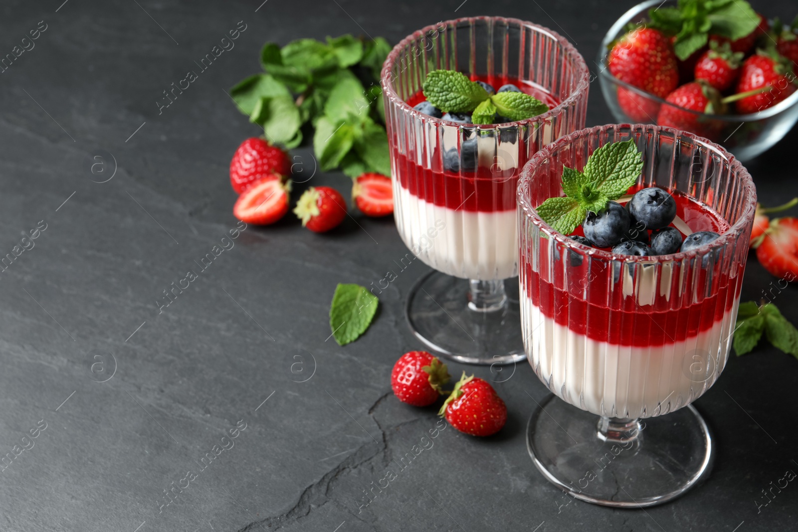 Photo of Delicious panna cotta with fruit coulis and fresh berries on dark grey table. Space for text