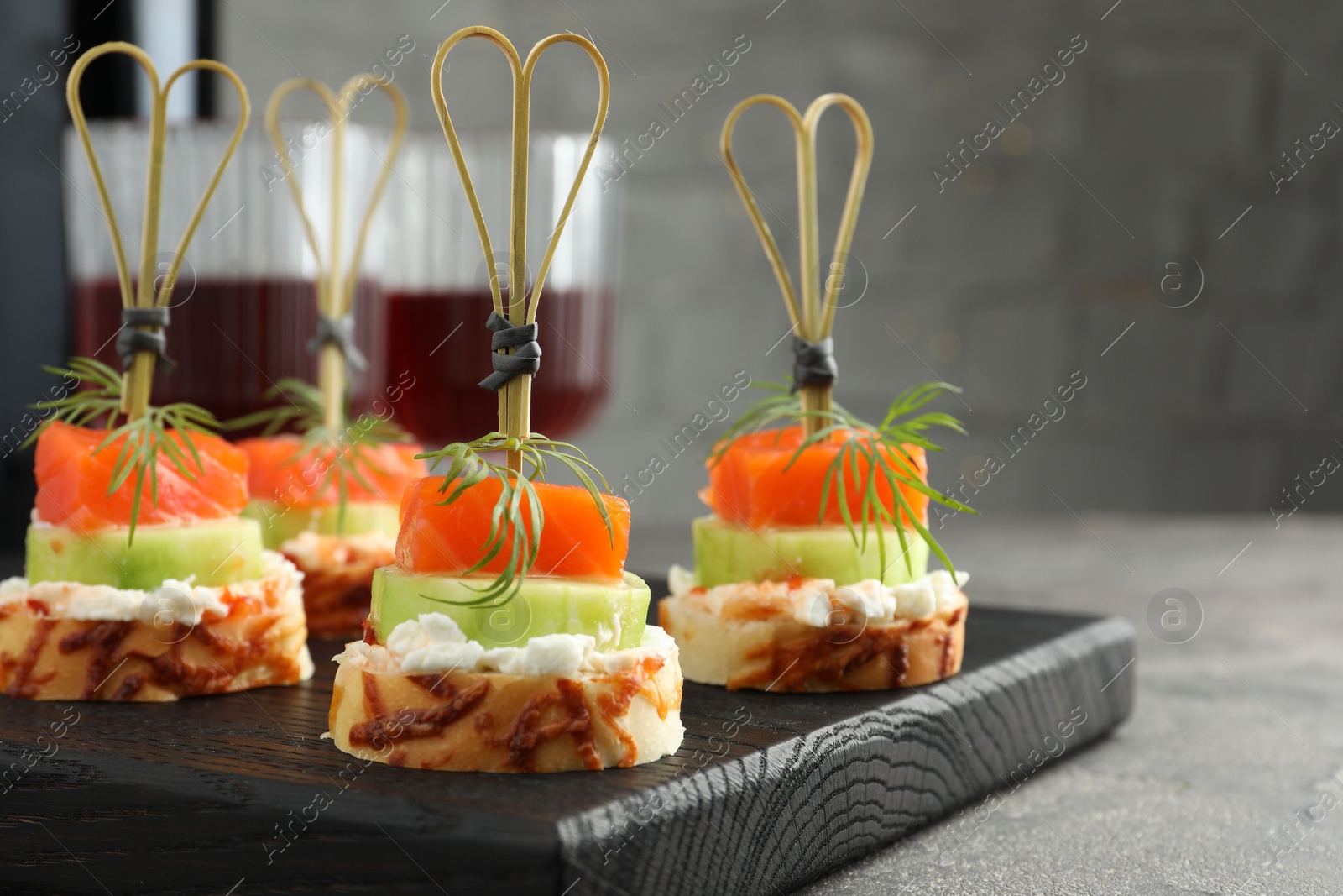 Photo of Tasty canapes with salmon, cucumber, bread and cream cheese served on grey table, closeup