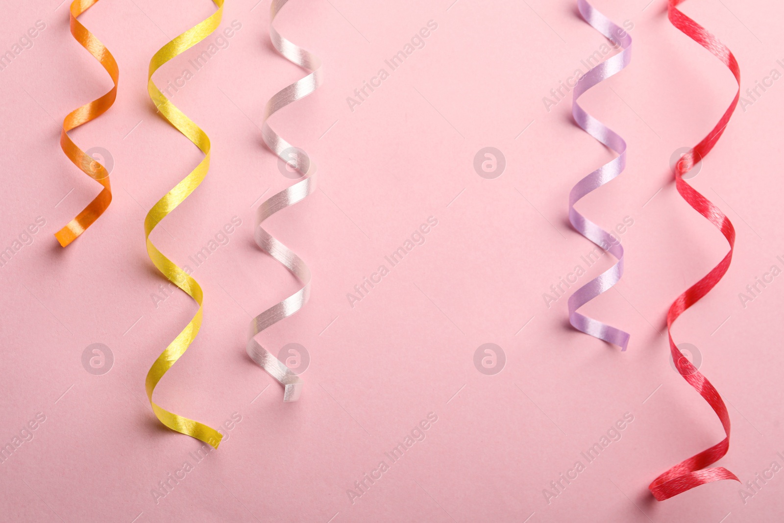 Photo of Colorful serpentine streamers on pink background, flat lay. Space for text