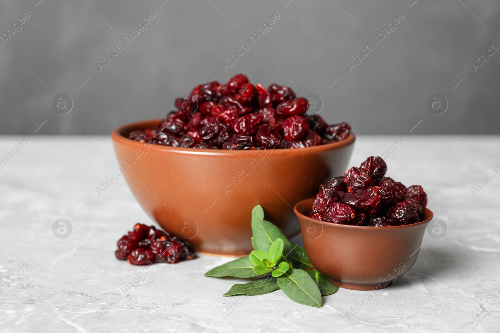 Photo of Tasty dried cranberries and leaves in bowls on grey table