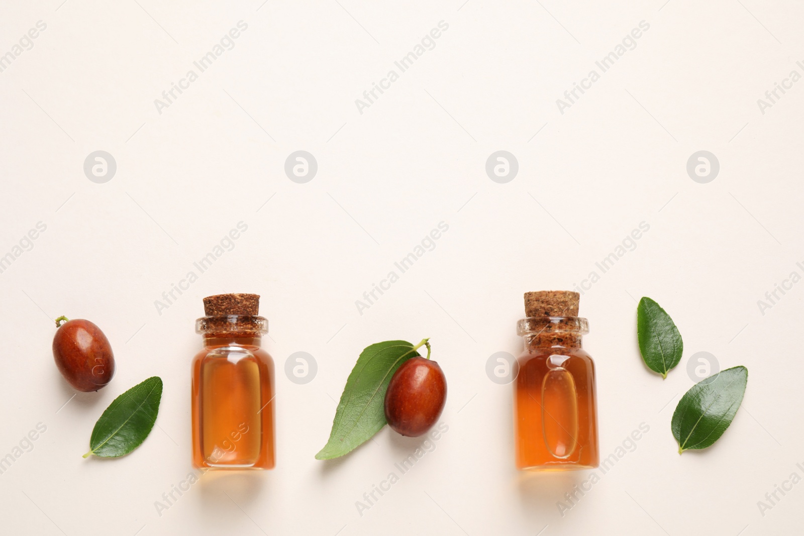 Photo of Glass bottles with jojoba oil and seeds on light background, flat lay. Space for text