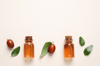 Glass bottles with jojoba oil and seeds on light background, flat lay. Space for text