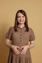 Happy young pregnant woman on light brown background