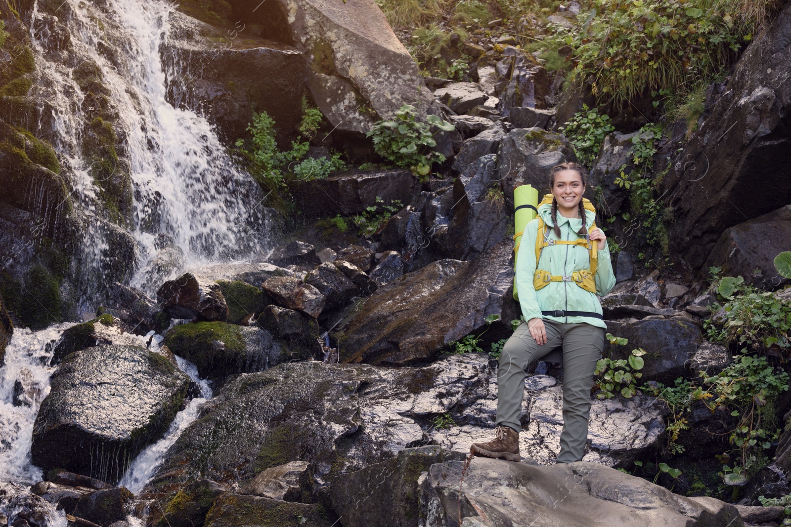 Photo of Tourist with backpack near waterfall in mountains. Space for text