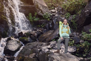 Photo of Tourist with backpack near waterfall in mountains. Space for text
