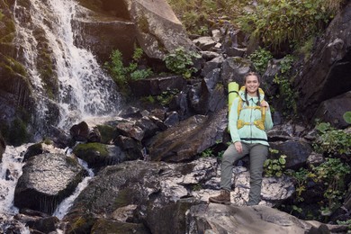 Tourist with backpack near waterfall in mountains. Space for text