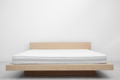 Photo of Comfortable bed with modern orthopedic mattress near white wall indoors