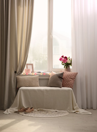 Comfortable place for rest with cushions and peony flowers near window indoors