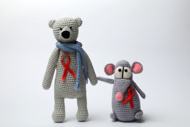 Photo of Cute knitted toys with red ribbons on light grey background. AIDS disease awareness