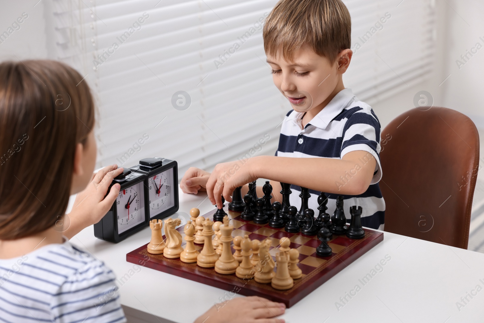 Photo of Cute children playing chess at table in room