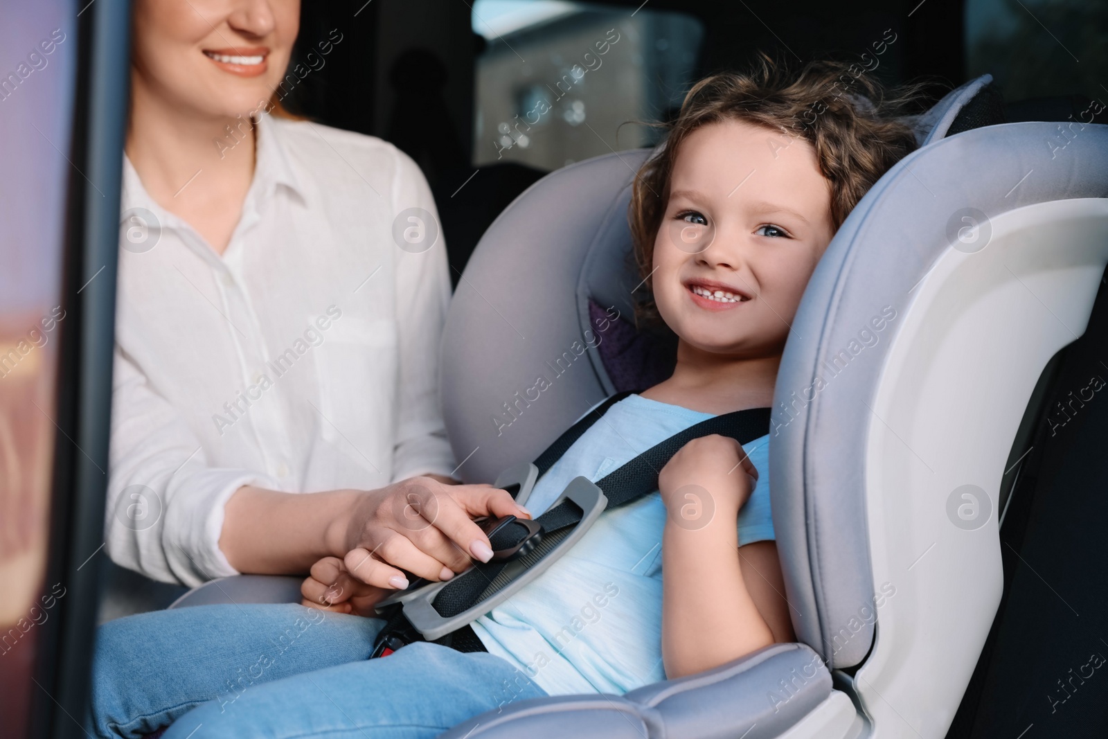 Photo of Mother fastening her daughter in child safety seat inside car