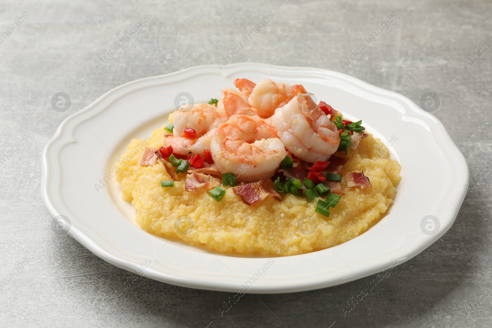 Photo of Plate with fresh tasty shrimps, bacon, grits, green onion and pepper on gray textured table, closeup