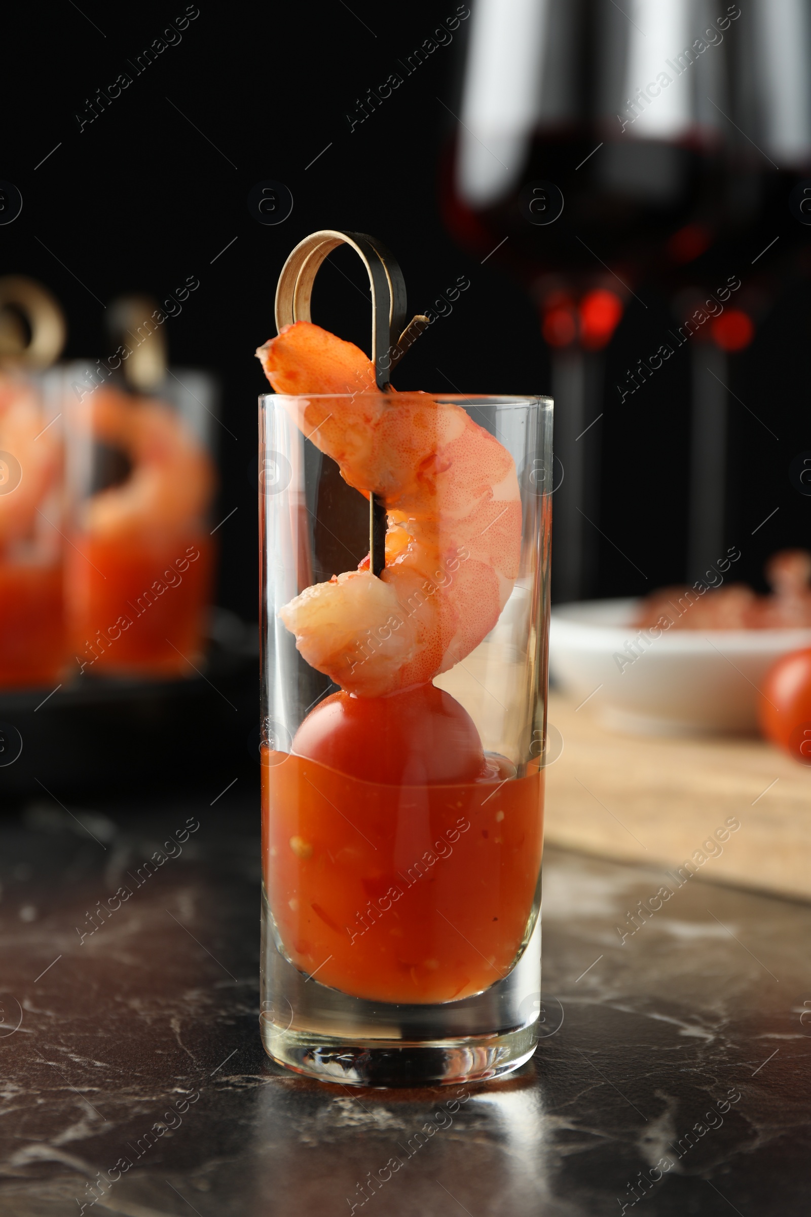 Photo of Tasty canape with shrimp, tomato and sauce in shot glass on black marble table, closeup