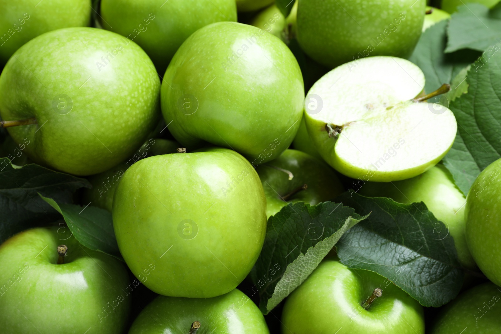 Photo of Pile of tasty green apples with leaves as background, closeup