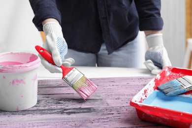Photo of Woman painting old plank with pink dye indoors, closeup