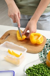 Photo of Woman cutting bell pepper and containers with fresh products on white table, closeup. Food storage