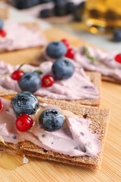 Photo of Tasty cracker sandwiches with cream cheese, blueberries, red currants and honey on wooden board, closeup