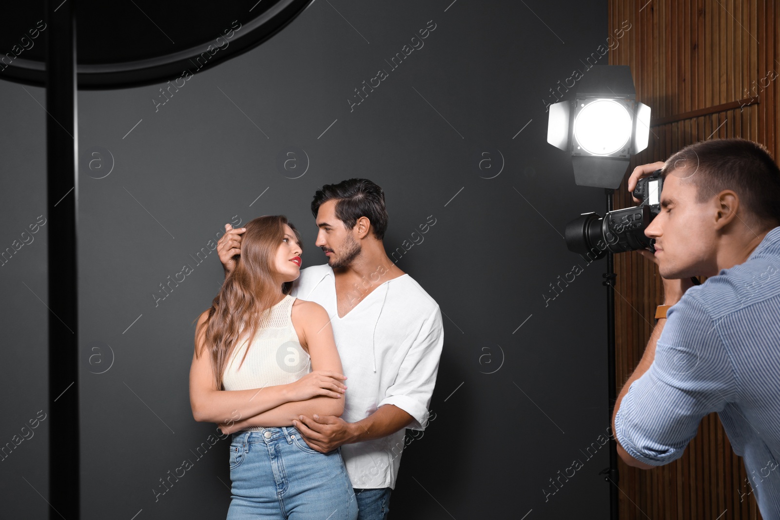 Photo of Professional photographer taking picture of young couple on dark grey background in modern studio