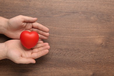 Photo of Man holding red decorative heart on wooden background, top view and space for text. Cardiology concept