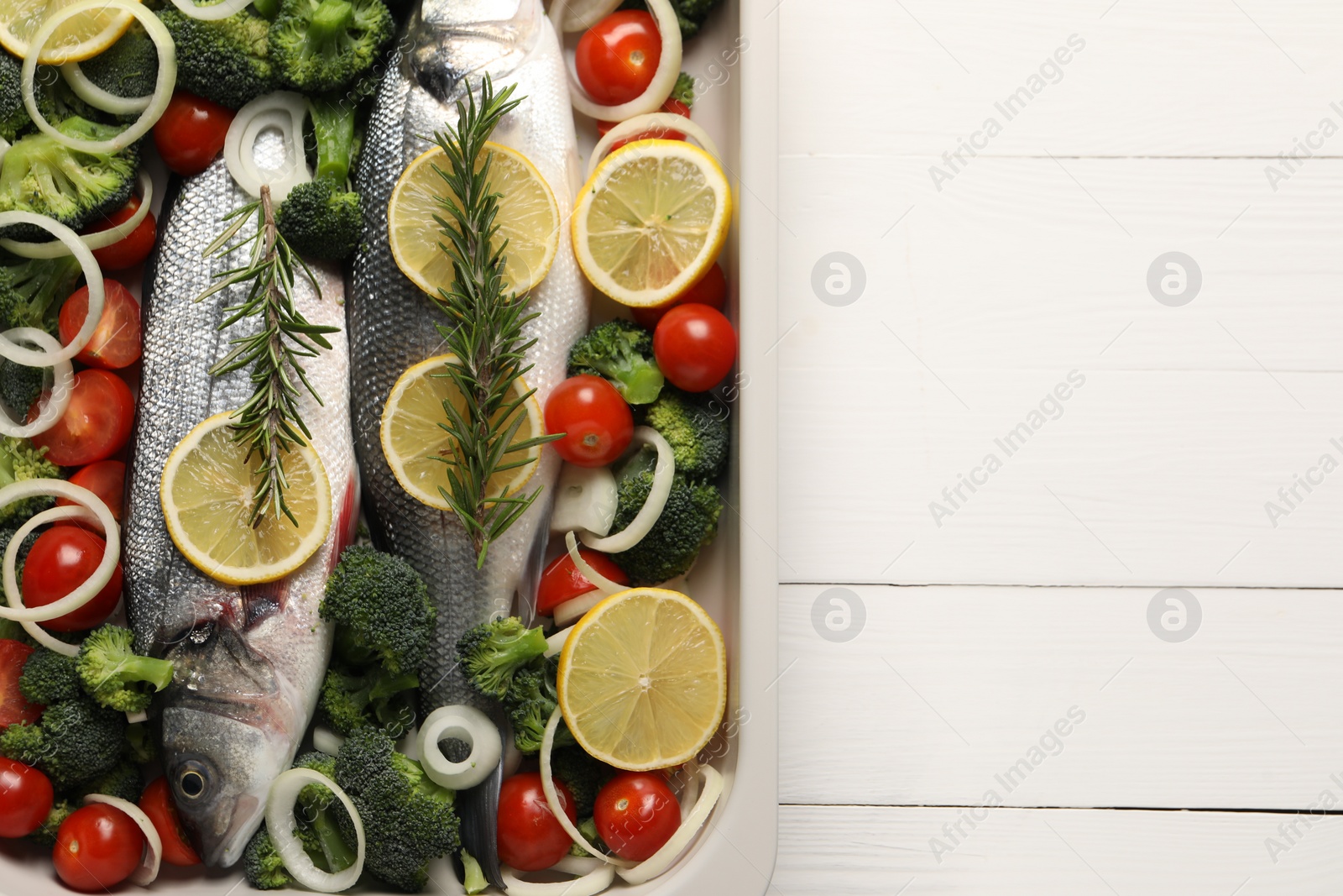 Photo of Raw fish with vegetables and lemon in baking dish on white wooden table, top view. Space for text