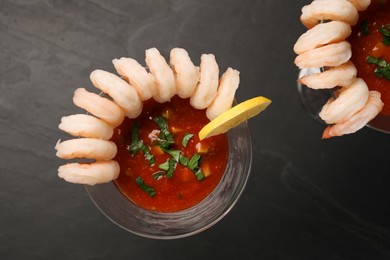 Tasty shrimp cocktail with sauce in glasses and lemon on grey textured table, flat lay