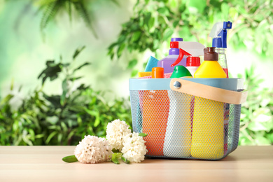 Photo of Spring flowers and basket with cleaning supplies on wooden table