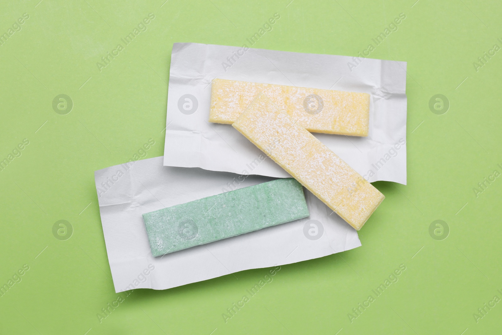 Photo of Sticks of tasty chewing gum on light green background, flat lay