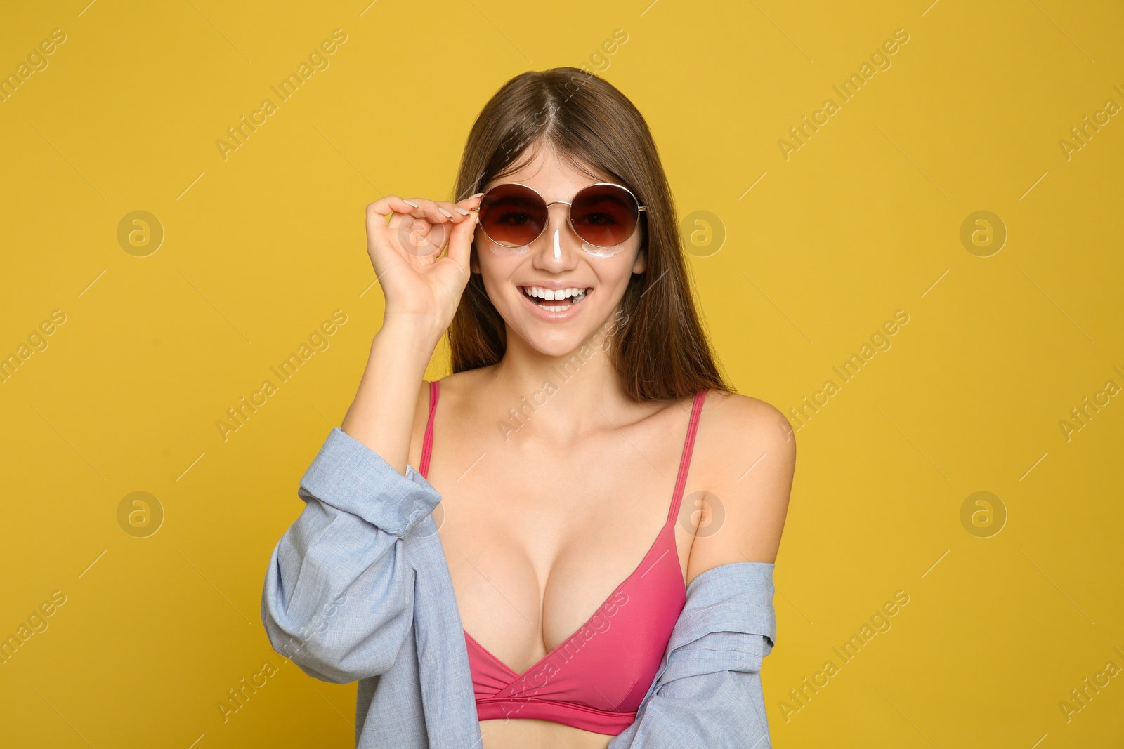 Photo of Teenage girl applying sun protection cream on her face against yellow background