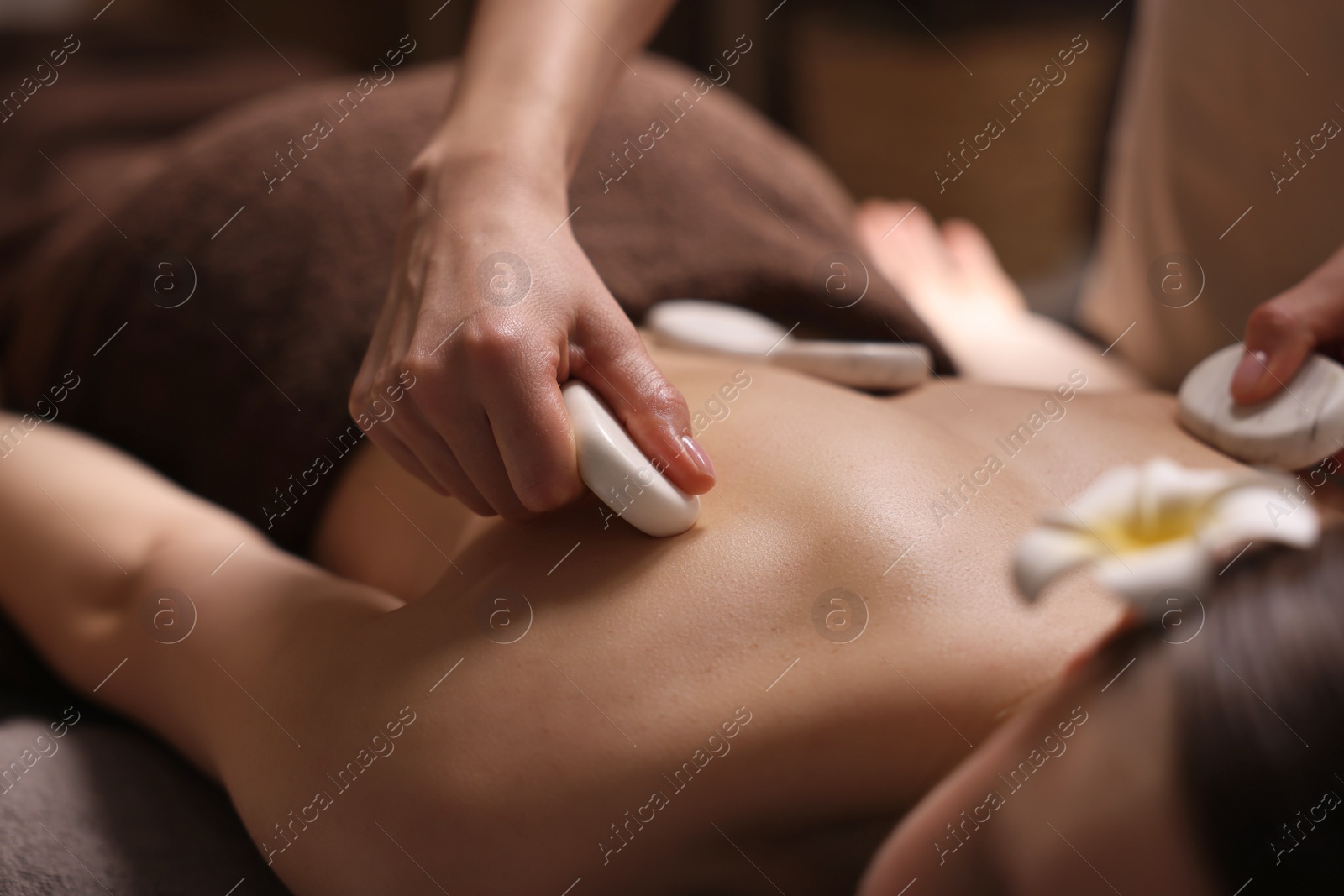 Photo of Spa therapy. Beautiful young woman lying on table during hot stone massage in salon, closeup