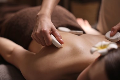 Spa therapy. Beautiful young woman lying on table during hot stone massage in salon, closeup