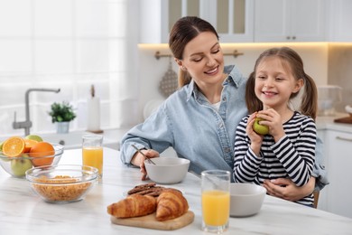 Mother and her cute little daughter having breakfast at table in kitchen