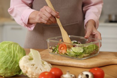 Woman cooking salad at wooden table in kitchen, closeup