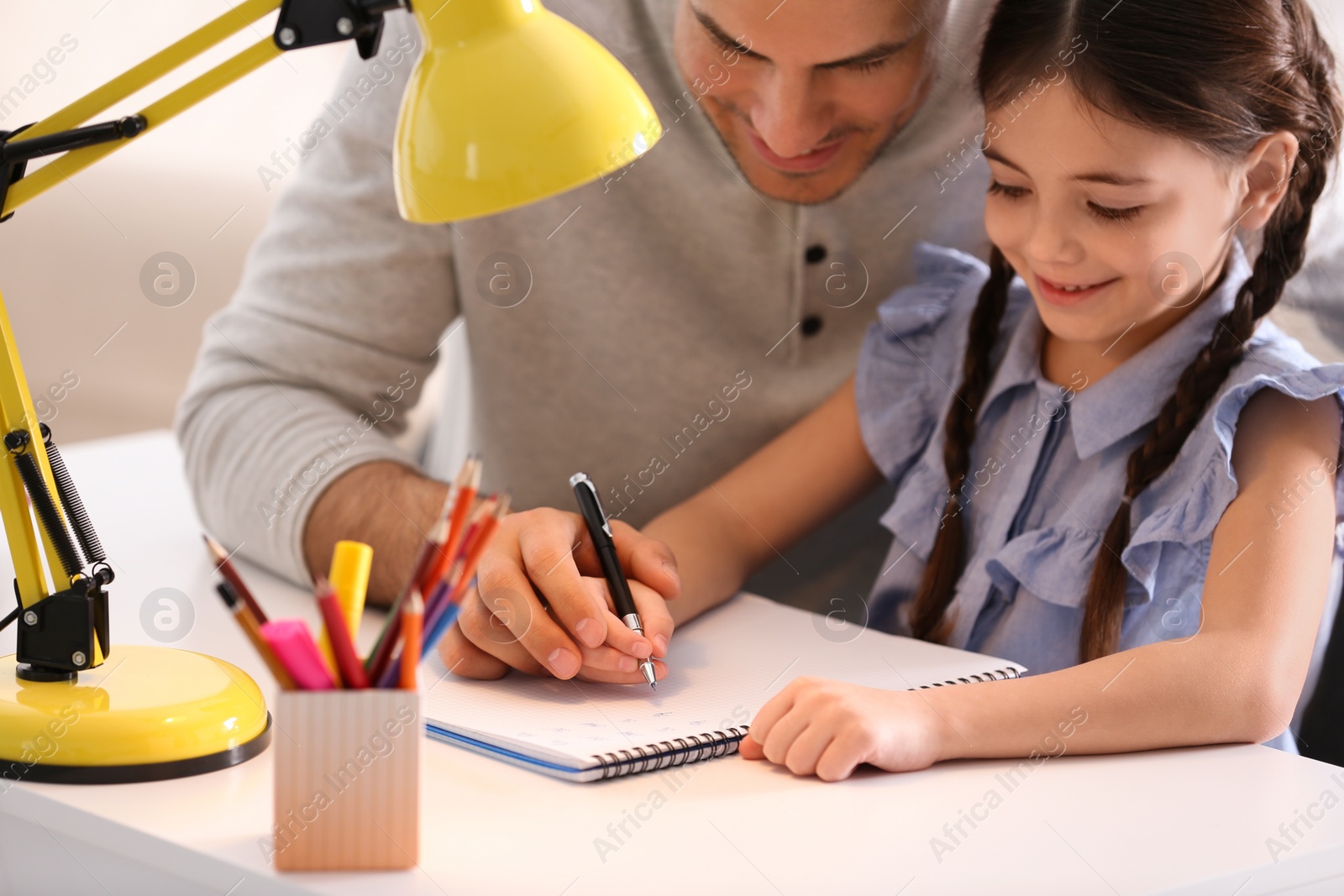 Photo of Man helping his daughter with homework at table indoors