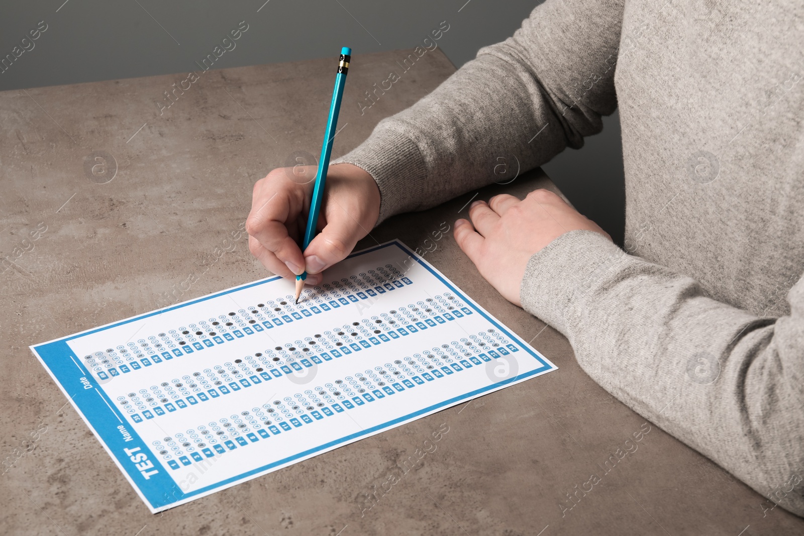 Photo of Student filling answer sheet at grey table, closeup. Passing exam