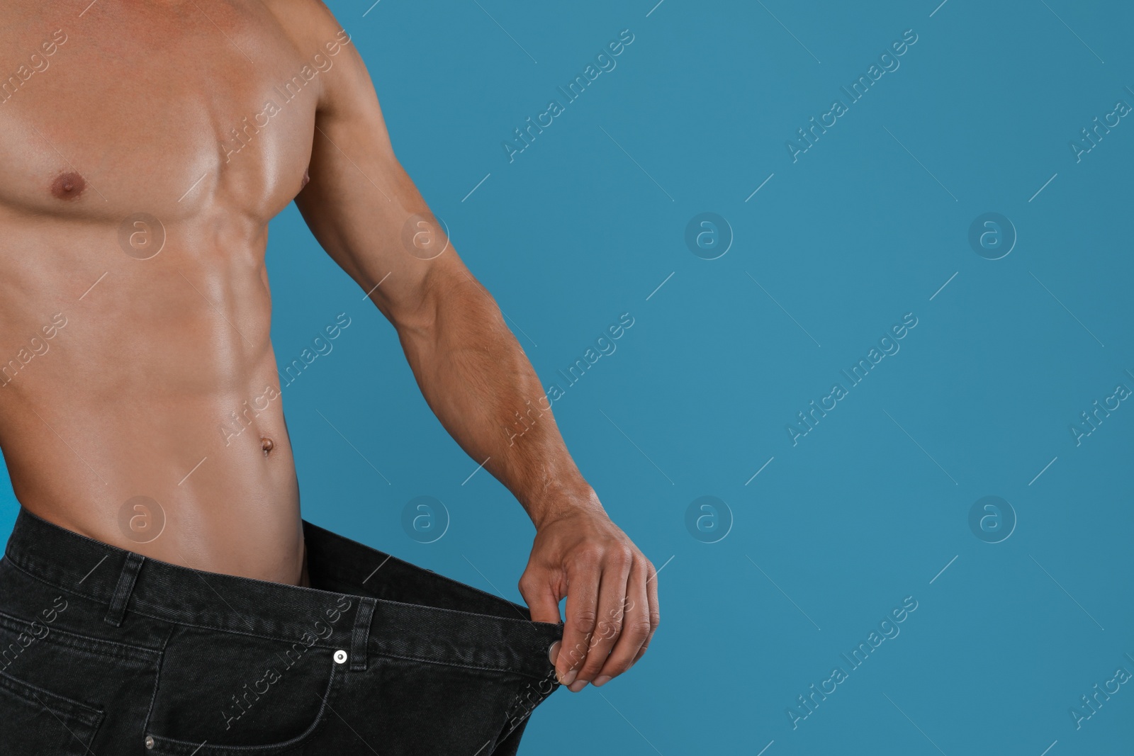 Photo of Shirtless man with slim body wearing big jeans on light blue background, closeup. Space for text