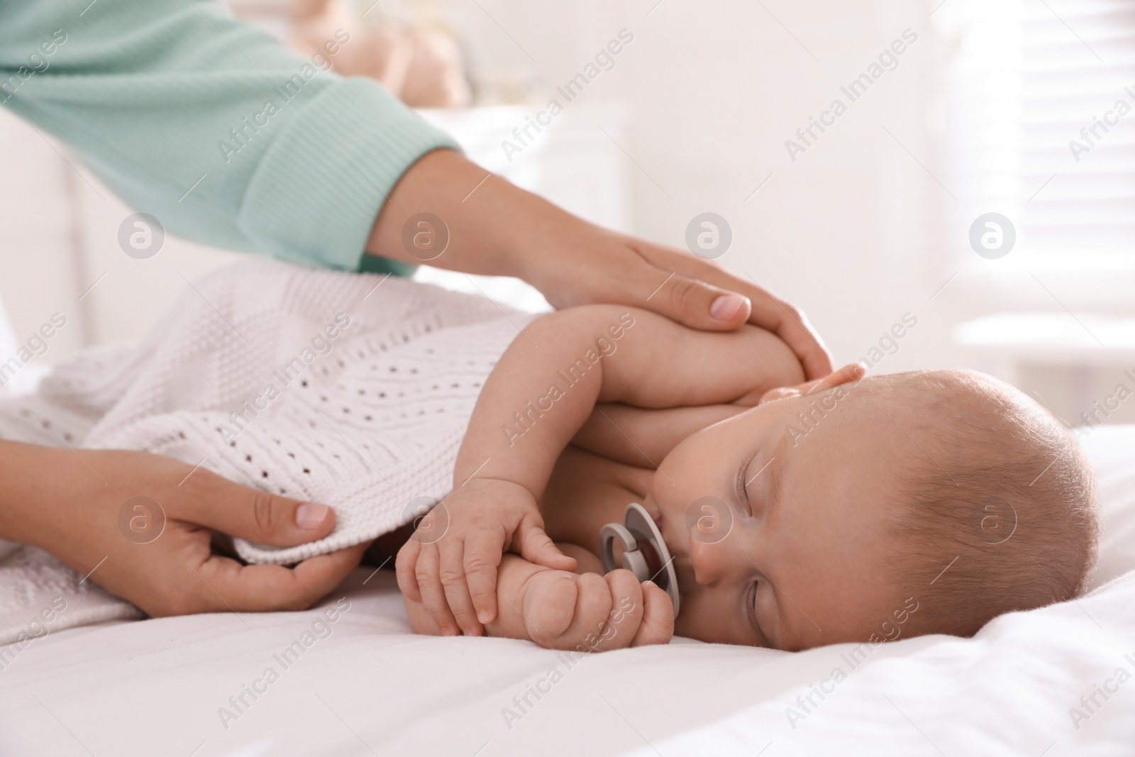 Photo of Mother covering her sleeping baby with knitted blanket at home
